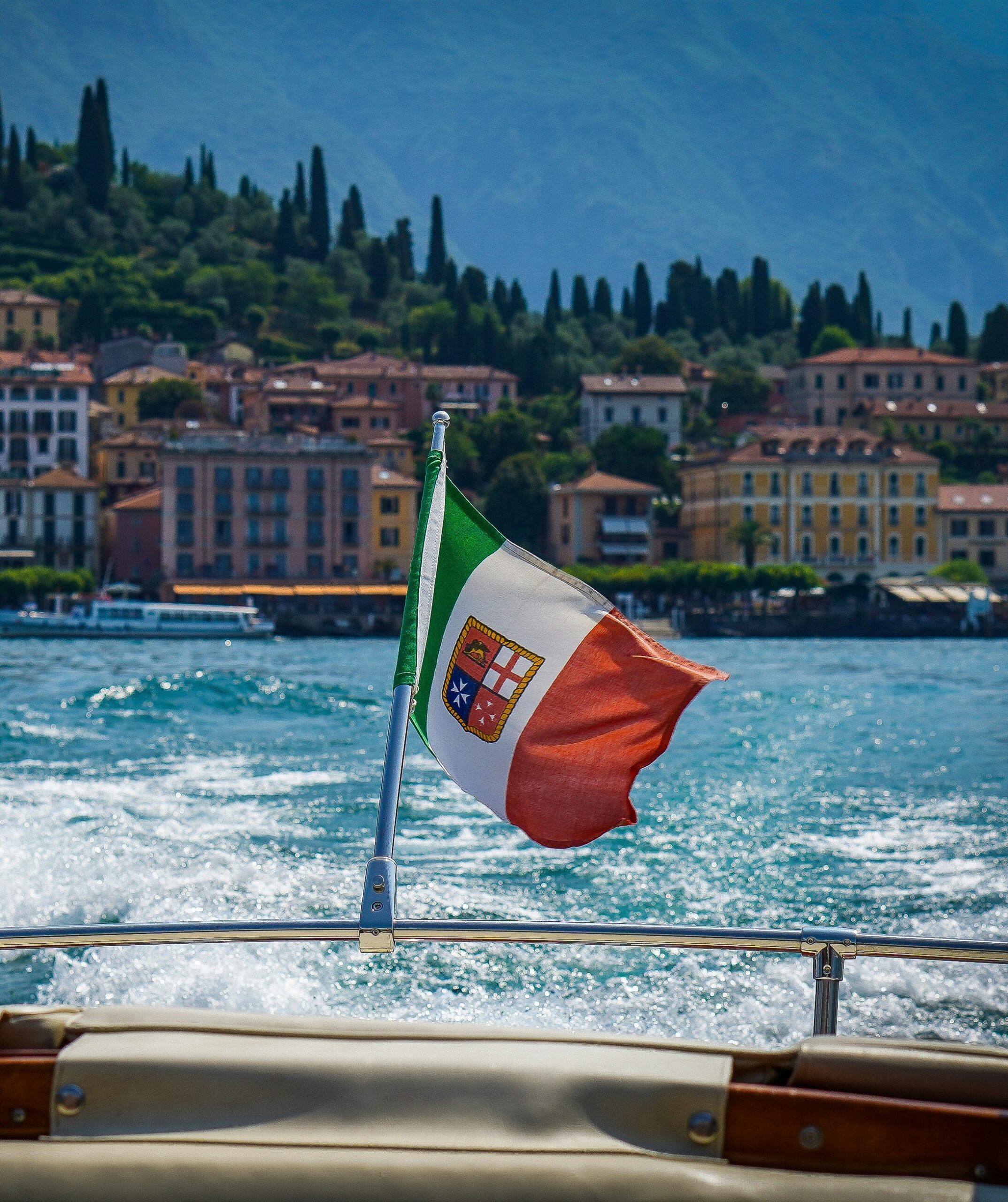 Private boat on Lake Como with the Italian flag in the foreground and Bellagio visible on the shoreline