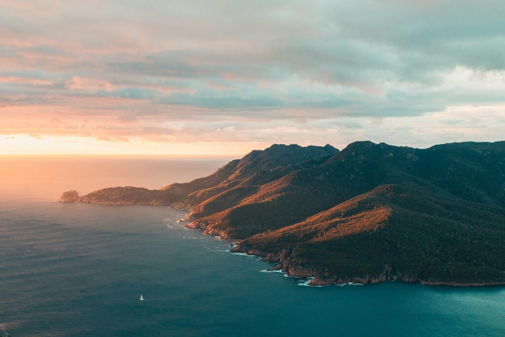 Tasmania's Freycinet coastline at sunset with a sailboat on the water
