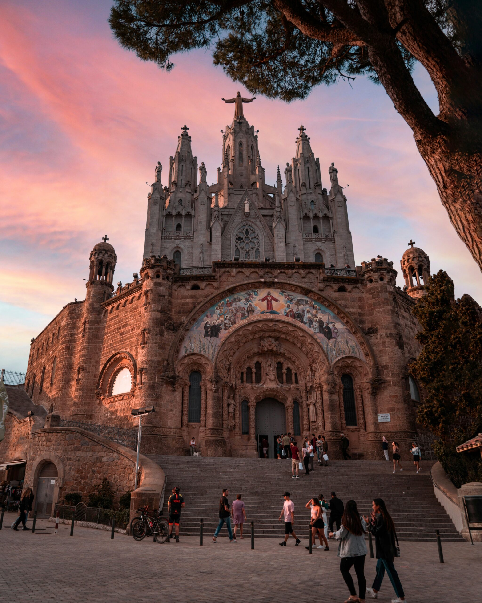 Sunset view of the Tibidabo church in Barcelona, Spain, with visitors gathered on the front steps